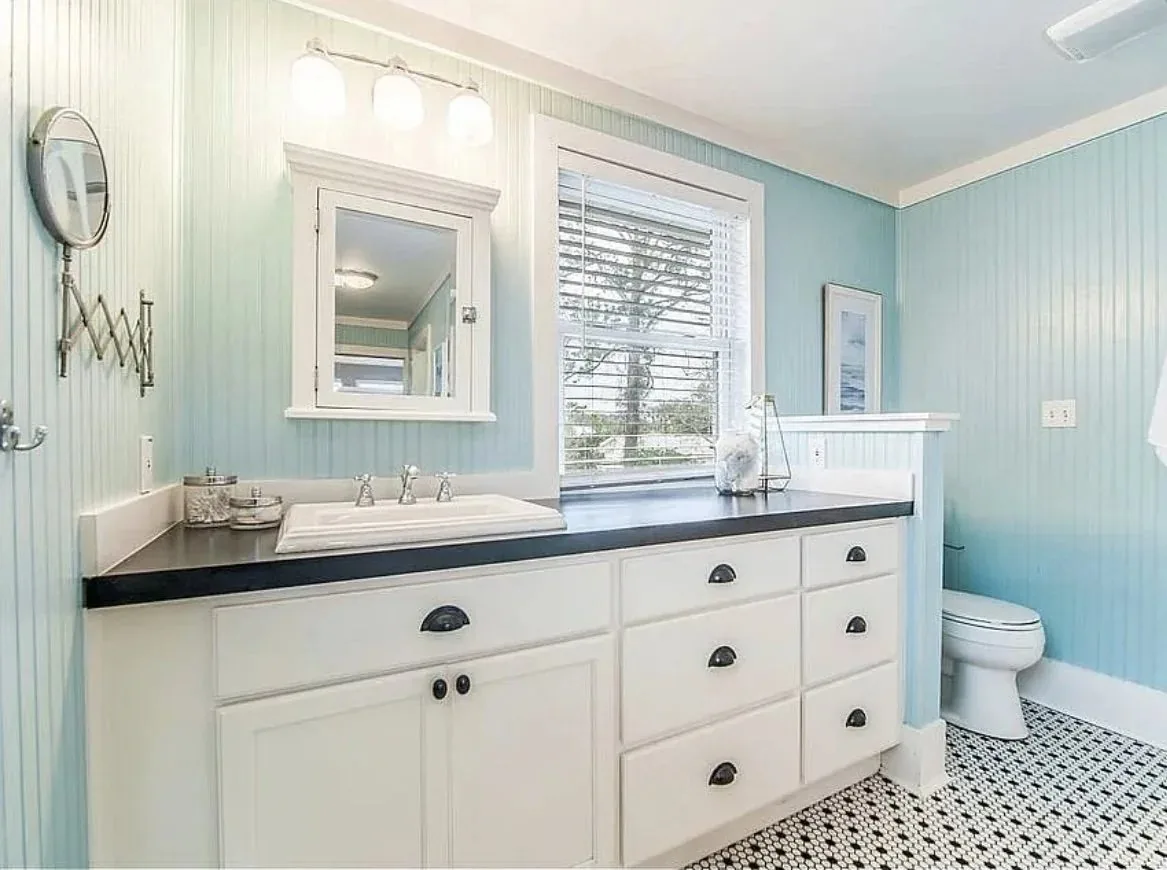 Bathroom with pale blue beadboard walls, a double vanity and patterned tile floor
