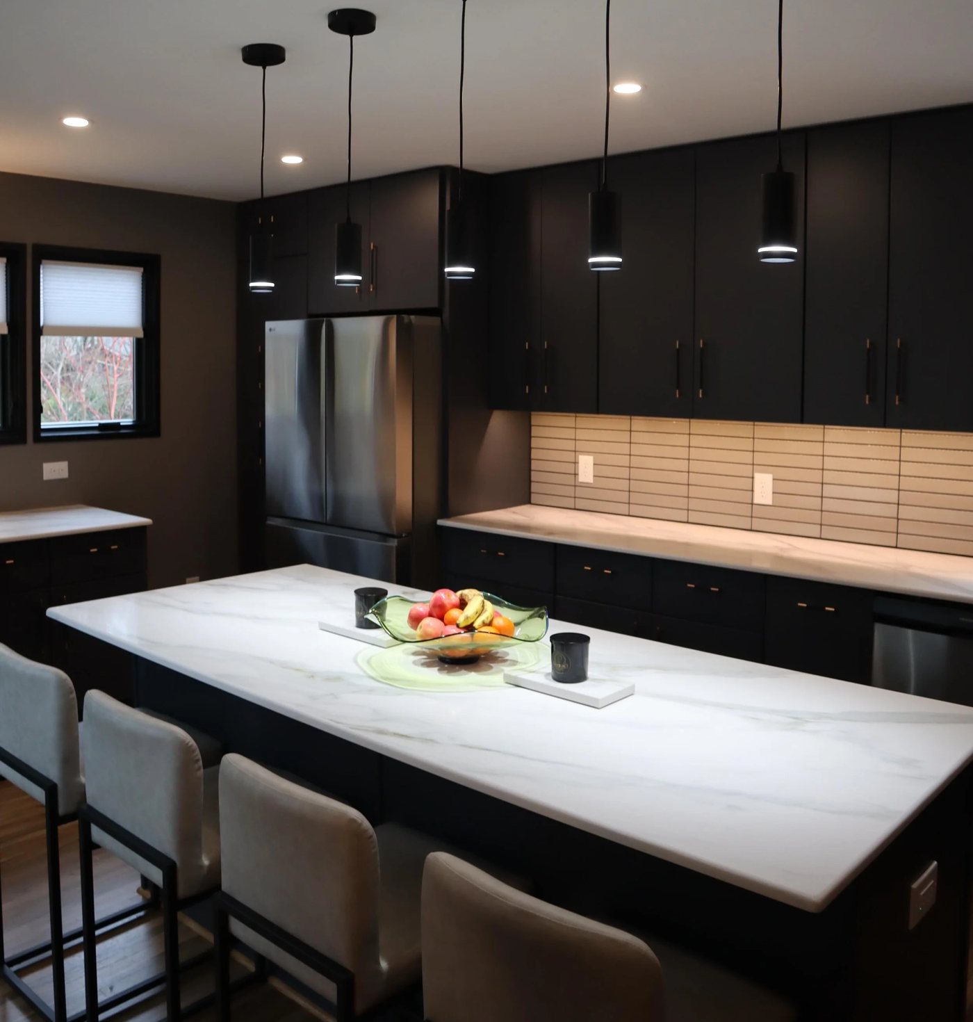 Dark cabinetry kitchen with a marble waterfall island and linear pendants