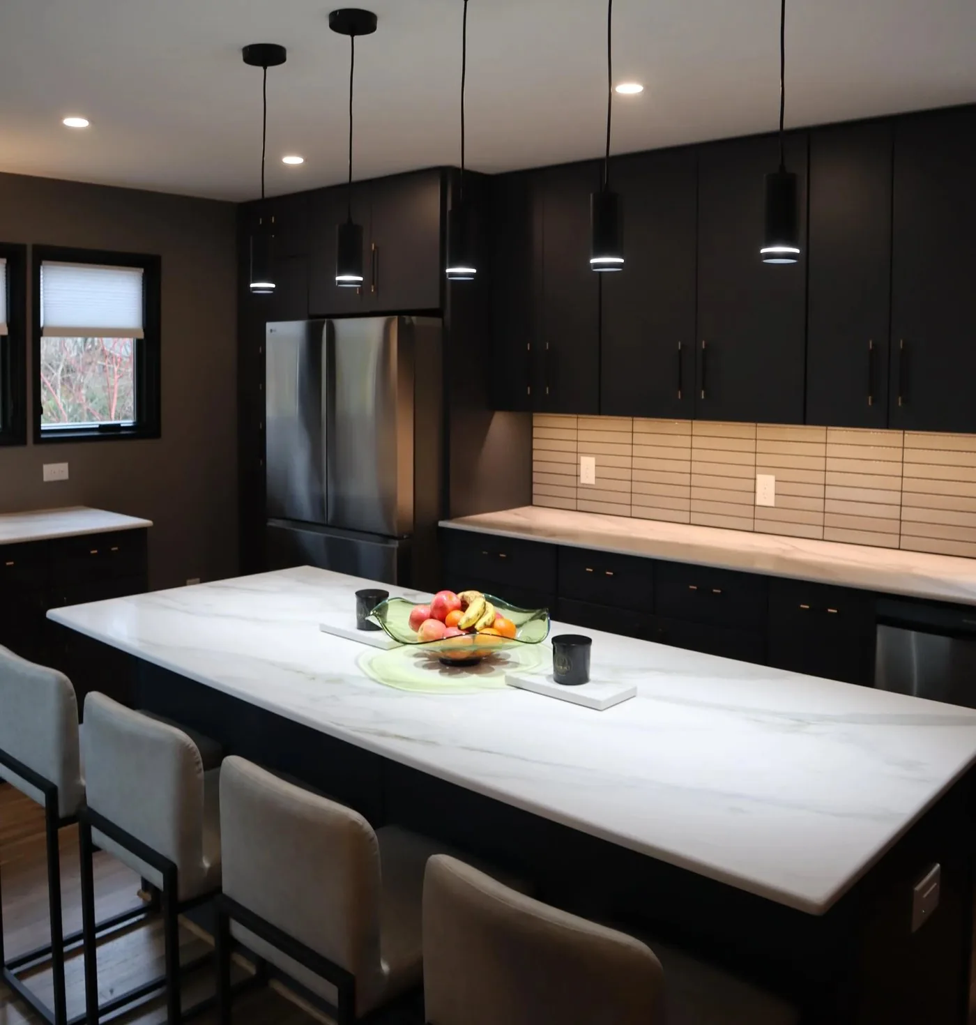 Dark cabinetry kitchen with a marble waterfall island and linear pendants